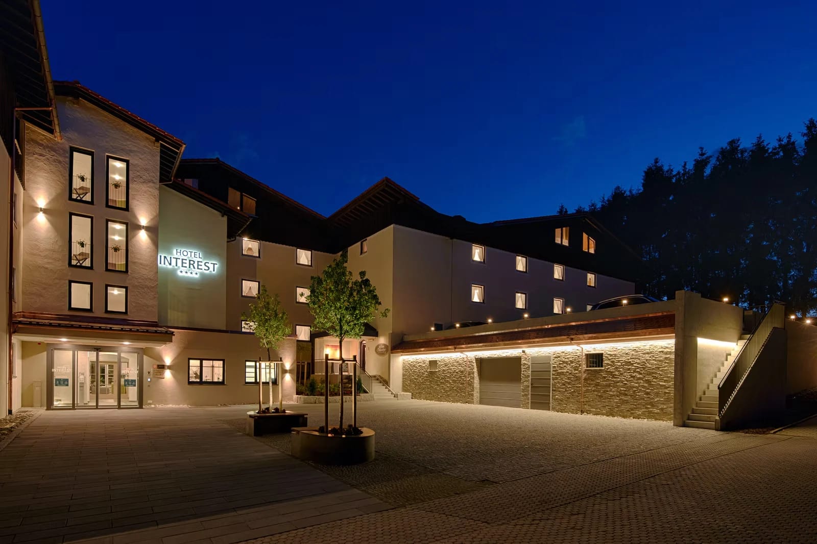 Beleuchtete Außenansicht des Hotels bei Nacht mit Innenhof und Eingang