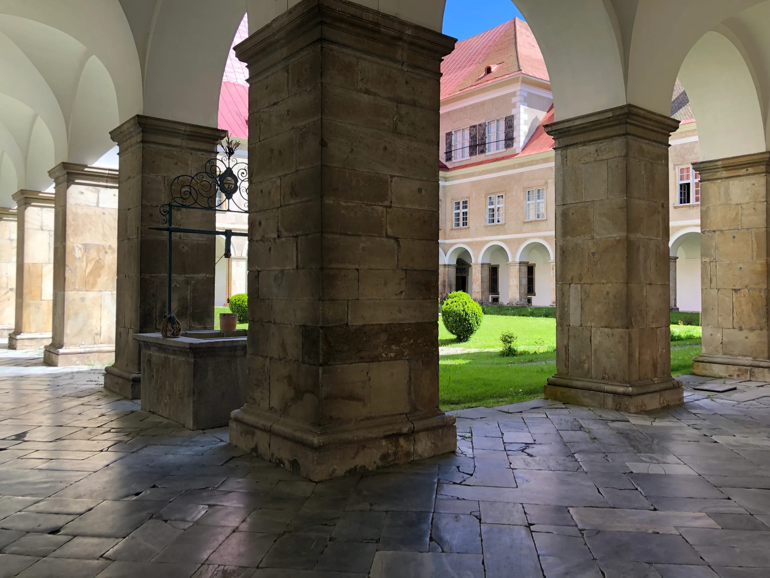 Arkadengang mit Sandsteinpfeilern und altem Brunnen, Blick in den begrünten Innenhof
