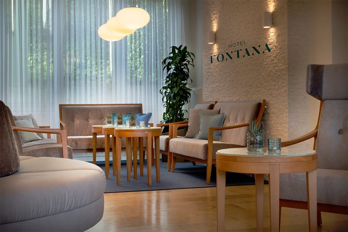 Helle Lounge mit Sesseln, Beistelltischen und dem Schriftzug Hotel Fontana an der Steinwand