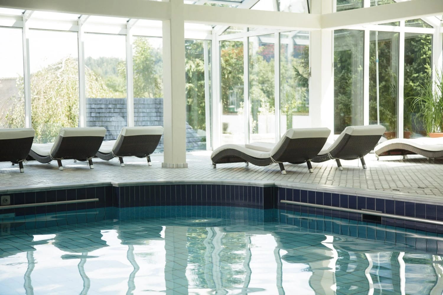 Innenpool mit Liegen und großer Glasfront zum Garten