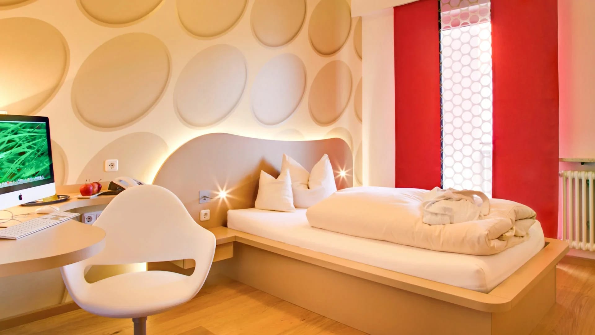 Design-Zimmer mit gemusterter Wandverkleidung, Bett, Schreibtisch mit Computer und rotem Vorhang