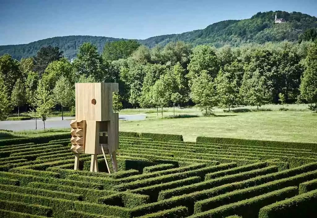 Heckenlabyrinth im Park mit hölzernem Aussichtsturm vor bewaldeten Hügeln