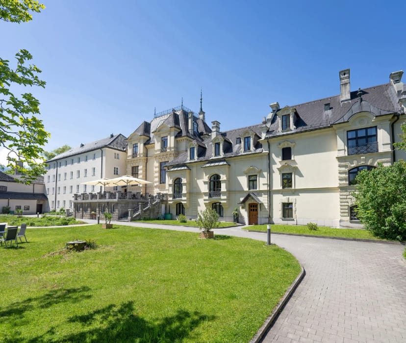 Historisches Schlossgebäude mit Erkertürmchen und Mansarddach, davor Rasenfläche und geschwungener Weg
