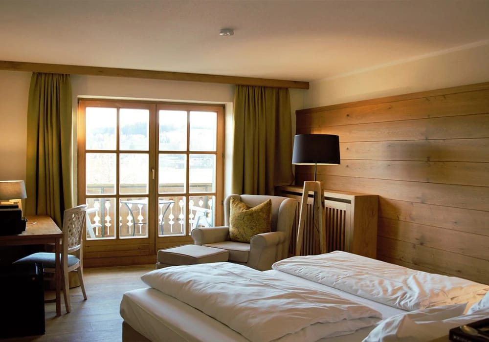 Zimmer mit Doppelbett, grünen Vorhängen und Balkontür mit Holzgeländer