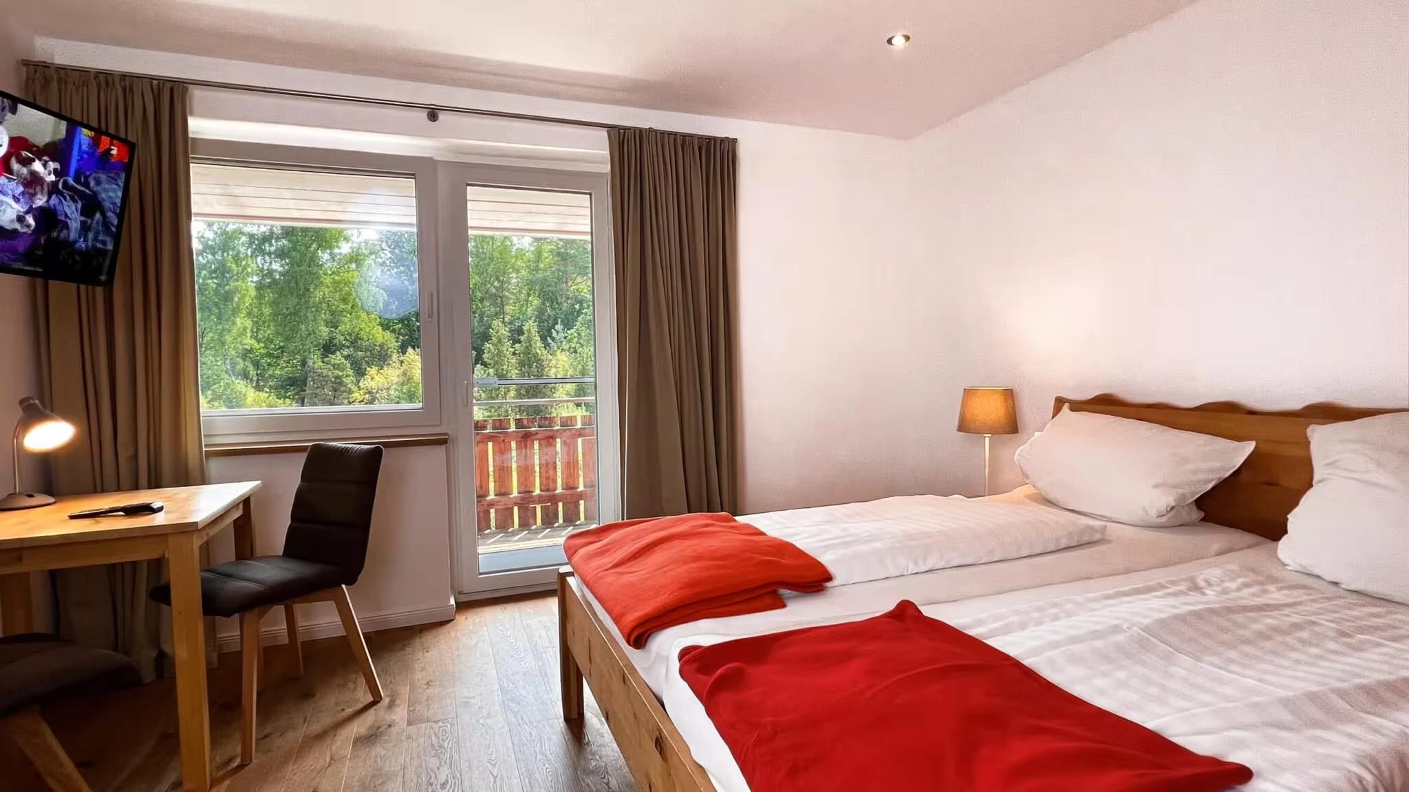 Doppelzimmer mit Holzbett, Schreibtisch und Balkontür ins Grüne