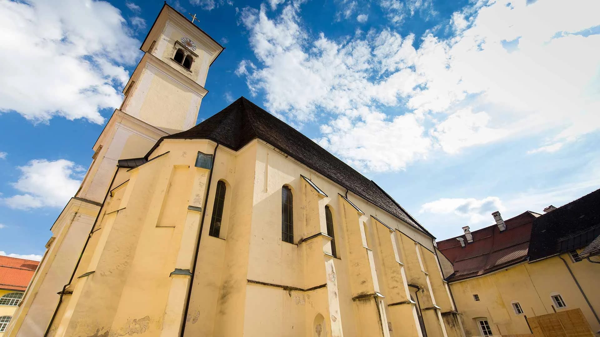 Ockerfarbene Stiftskirche mit Glockenturm und Strebepfeilern unter blauem Himmel
