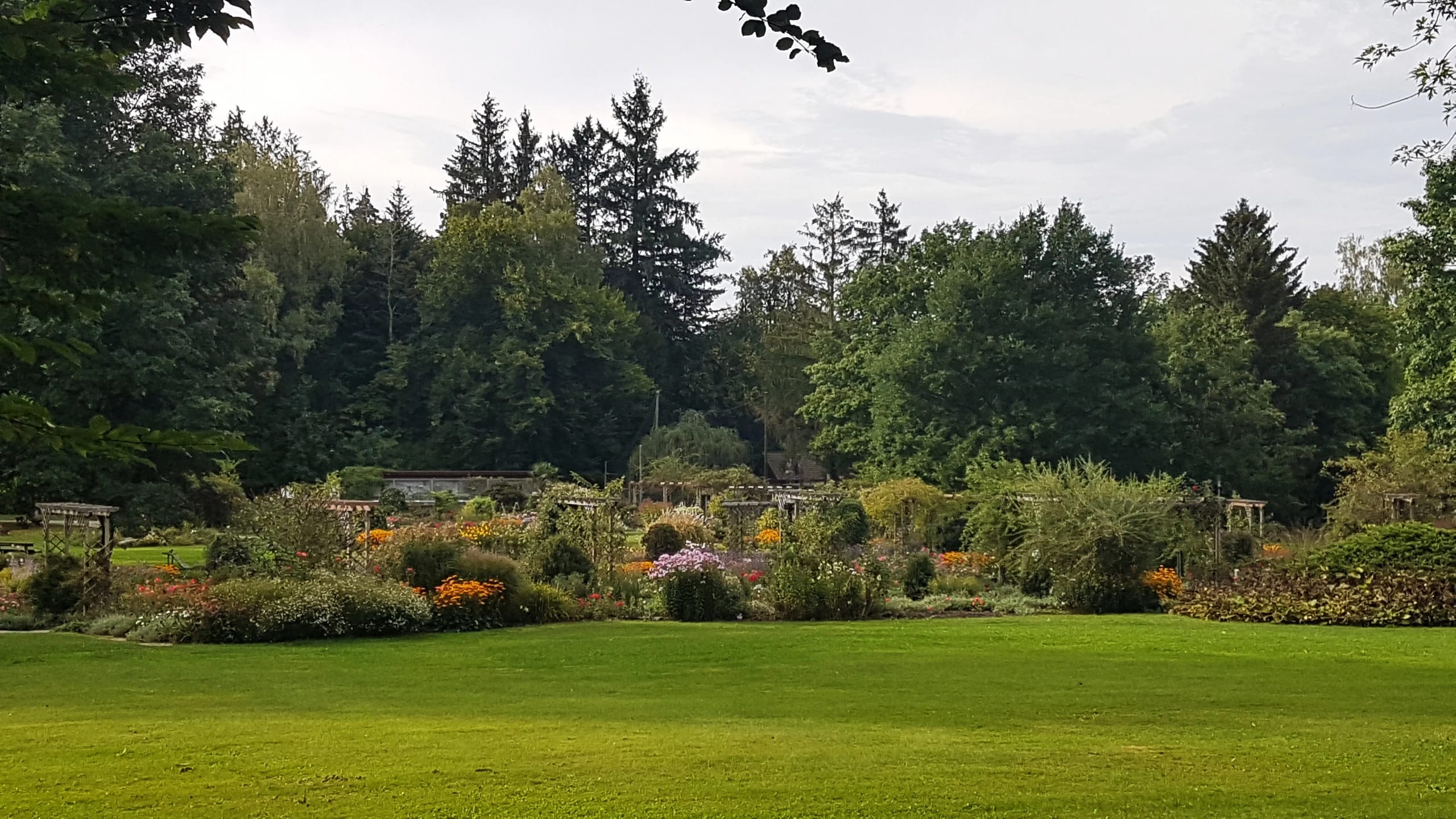 Kurpark mit weiter Rasenfläche, bunten Blumenbeeten und hohen Bäumen