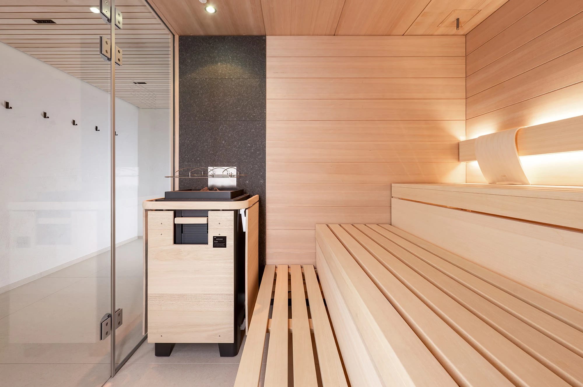 Sauna mit hellen Holzbänken, Saunaofen und Glastür
