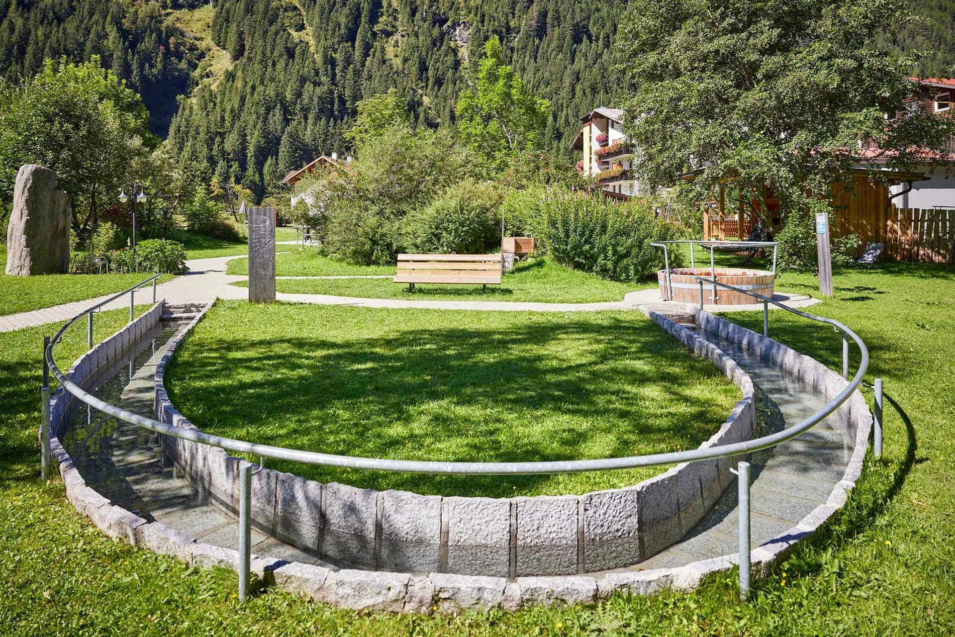 Kneippanlage im Garten mit Wassergraben, Wiese und Bergen im Hintergrund