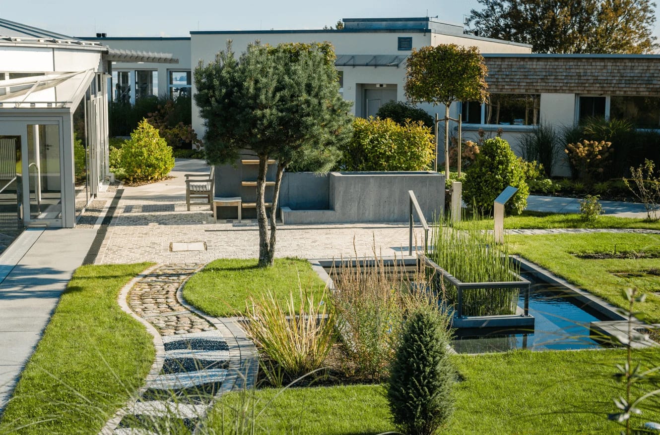 Gartenanlage mit Wassertretbecken, Kiespfaden und Sitzplatz vor den flachen Klinikgebäuden