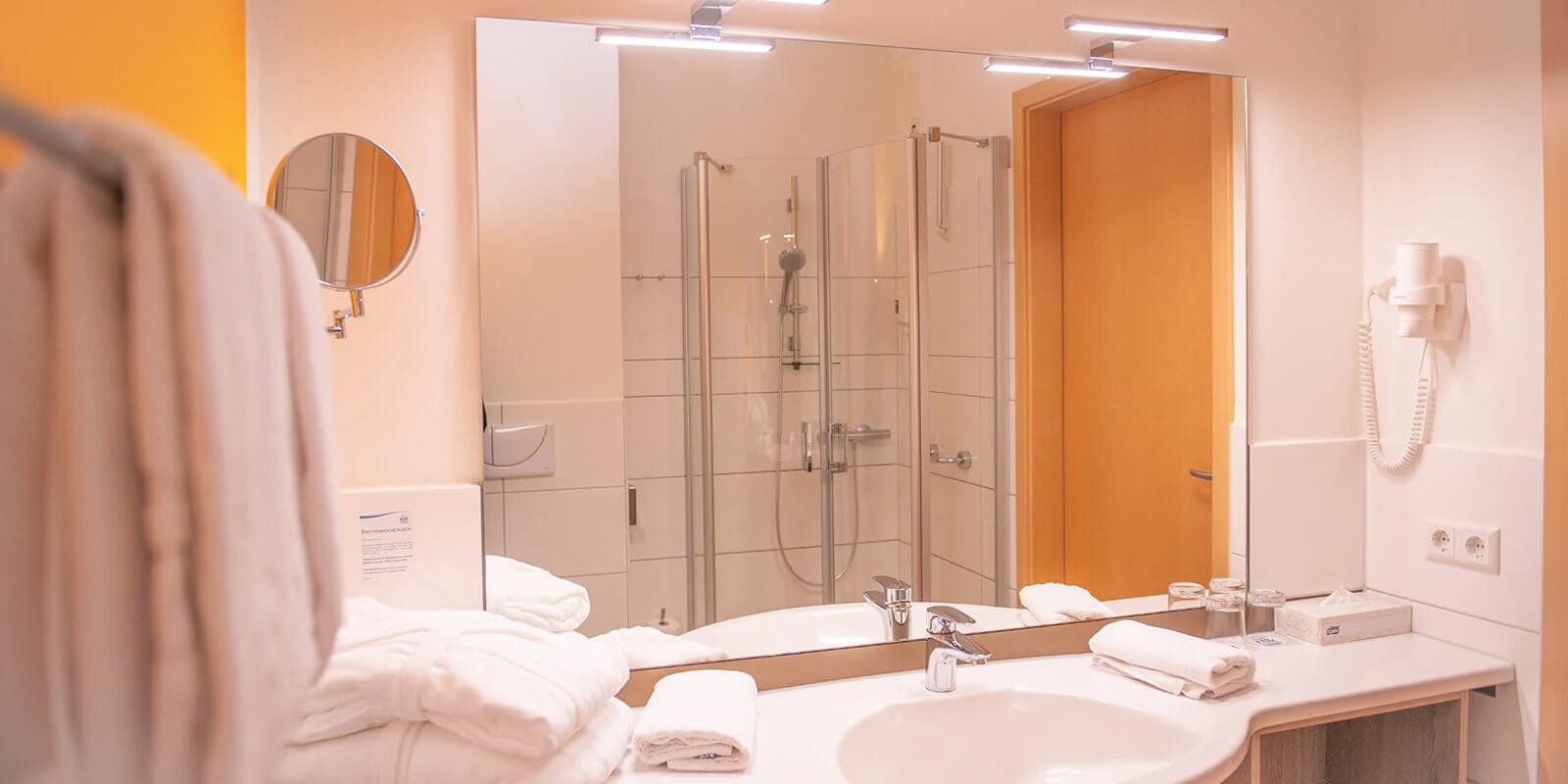 Badezimmer mit Dusche, breitem Waschtisch, Spiegel und Handtüchern