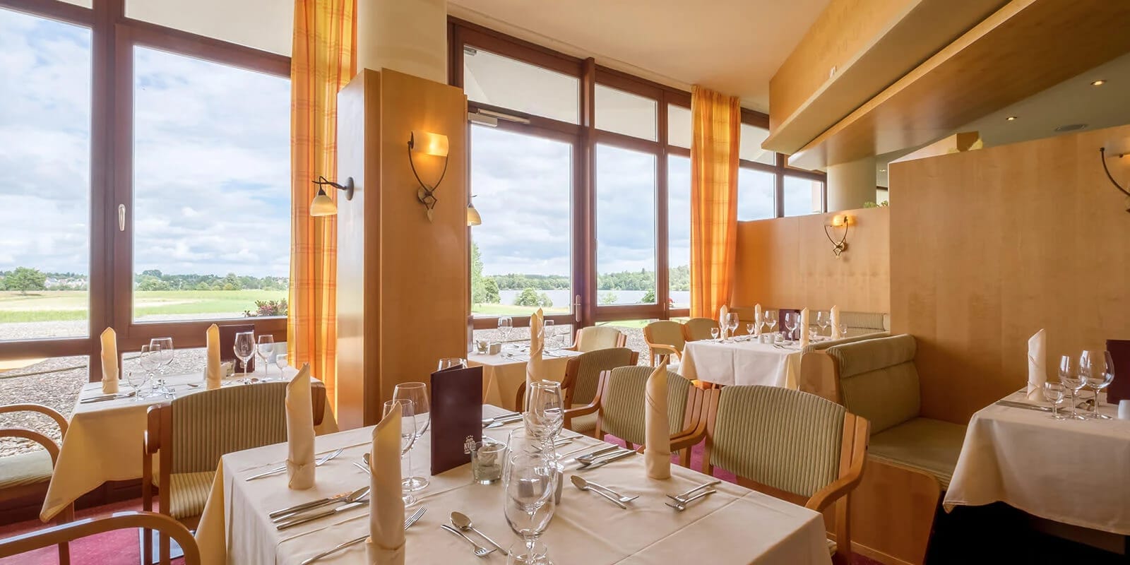 Restaurant mit eingedeckten Tischen und Fensterfront ins Grüne