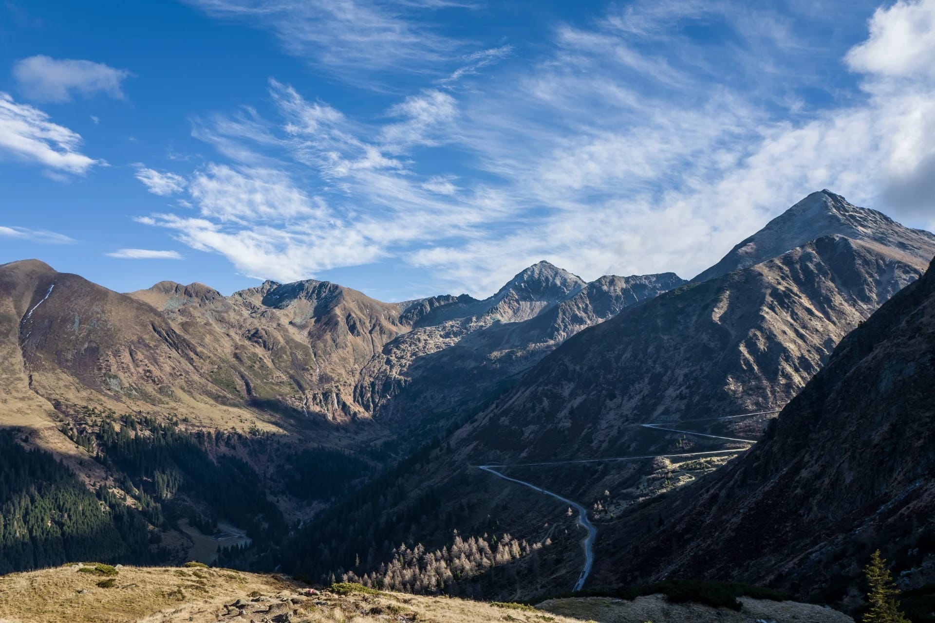 Blick über ein Bergtal mit Gipfeln, Wiesen und blauem Himmel