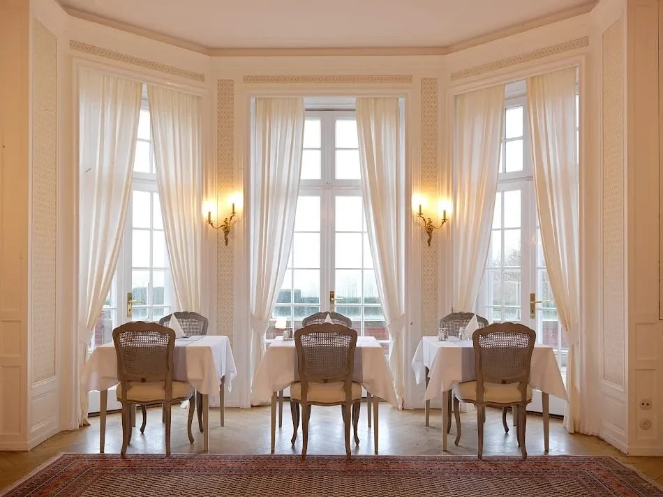 Speisesaal mit eingedeckten Tischen an hohen Erkerfenstern