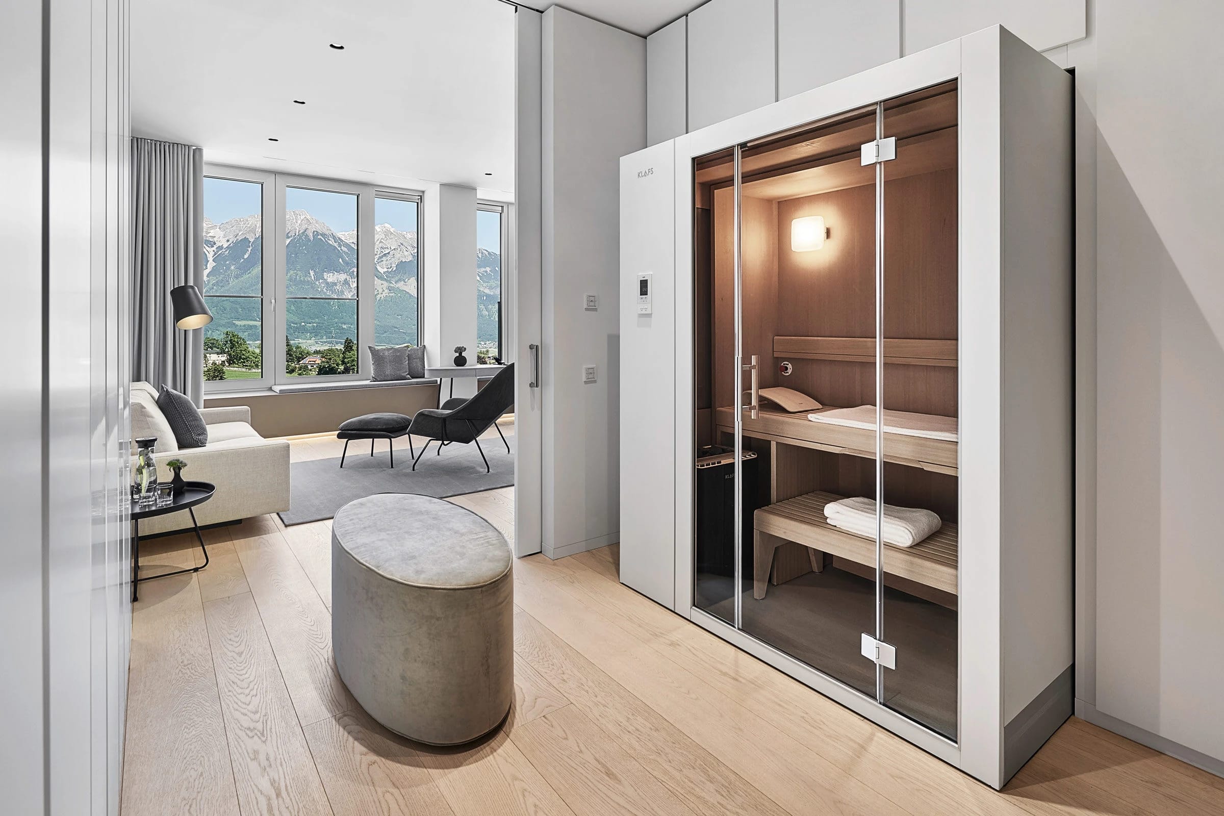 Sauna mit Glasfront in der Suite, dahinter der Wohnbereich mit Fensterfront und Bergblick