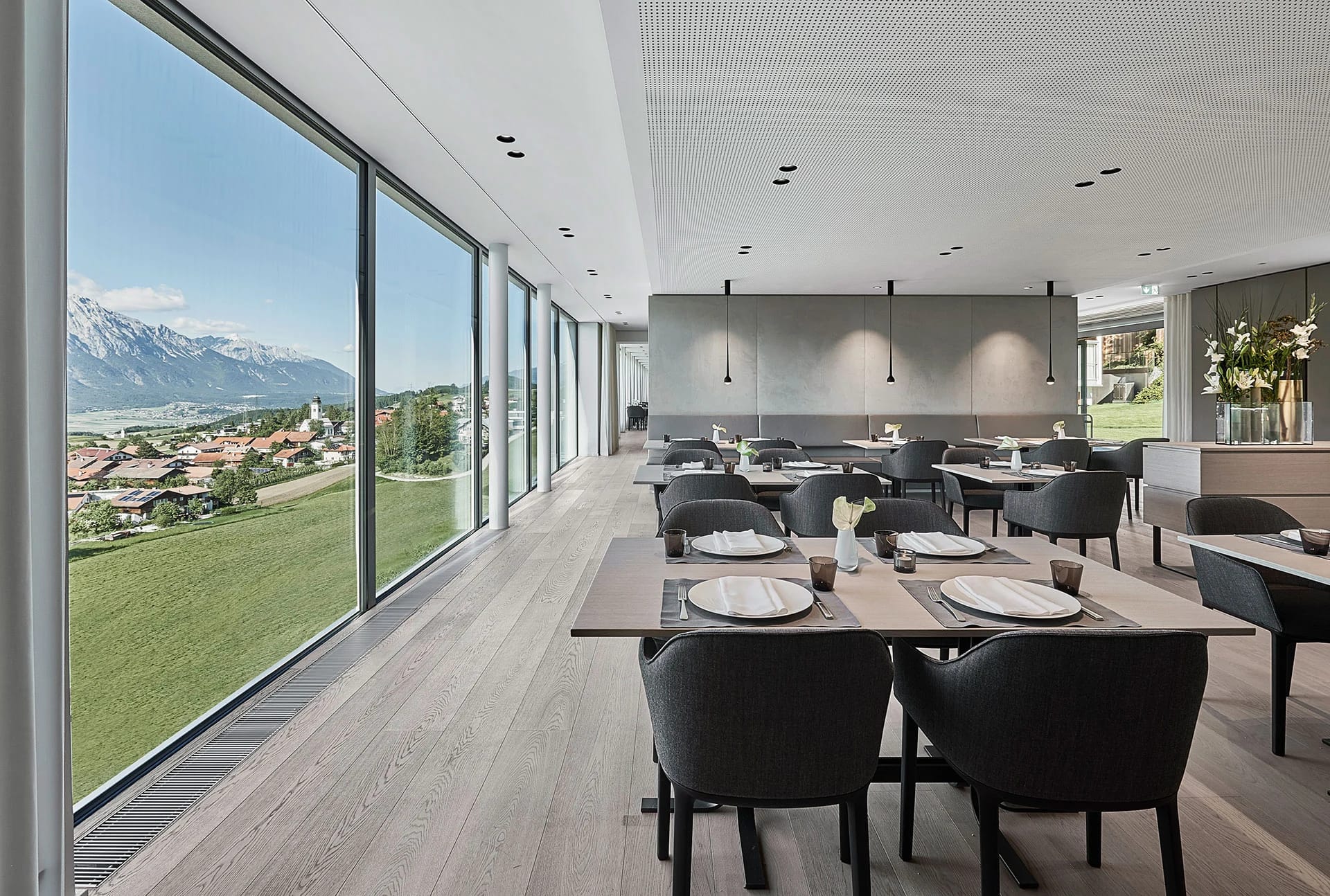 Restaurant mit eingedeckten Tischen und Panoramafenster über Dorf und Berge