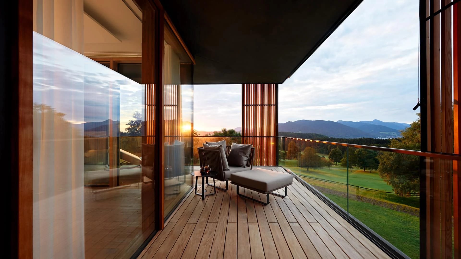 Holzbalkon mit Liegesessel und Blick über Wiesen und Berge im Abendlicht