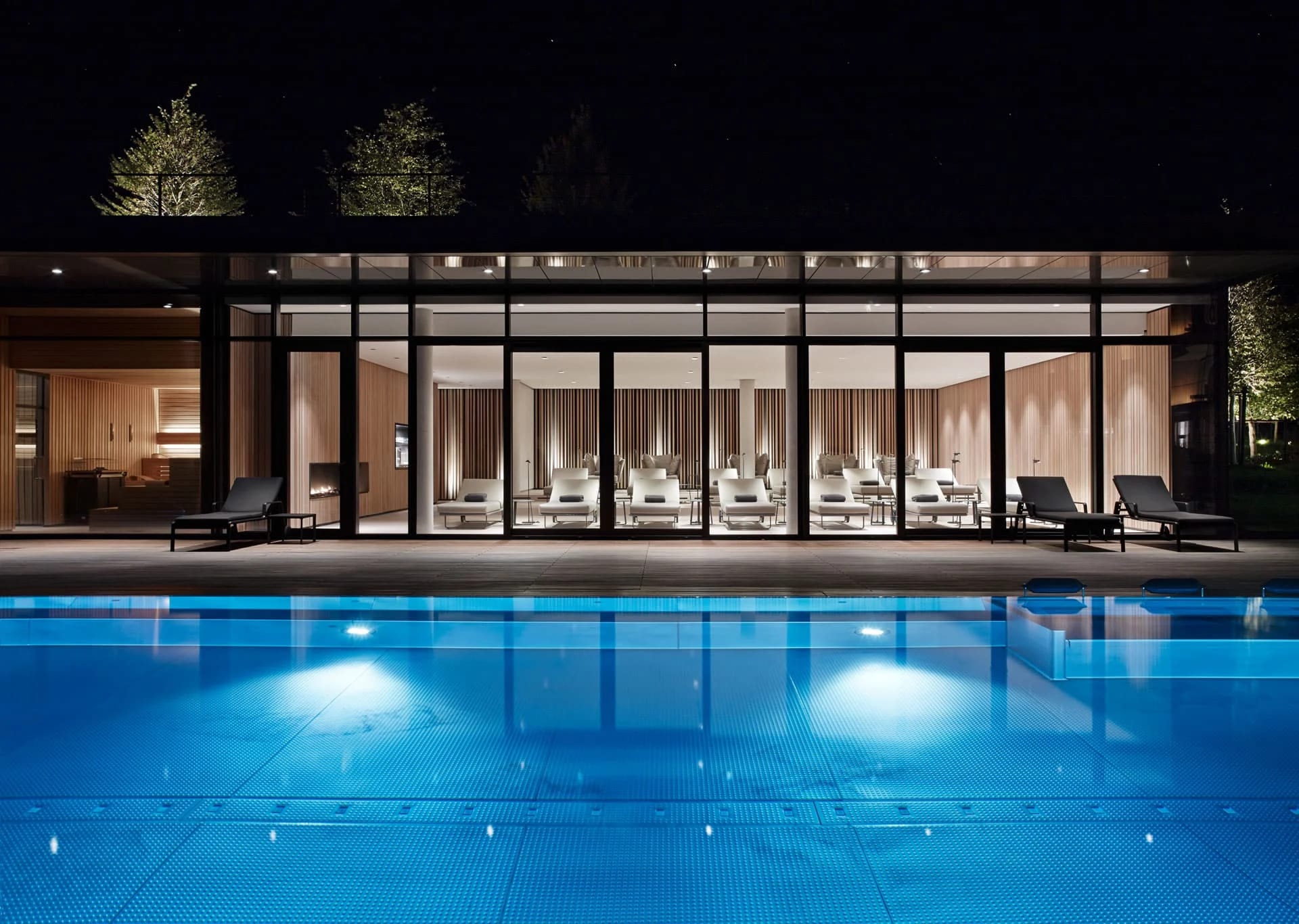 Beleuchtetes Poolhaus mit Glasfront und Liegen am Außenpool bei Nacht
