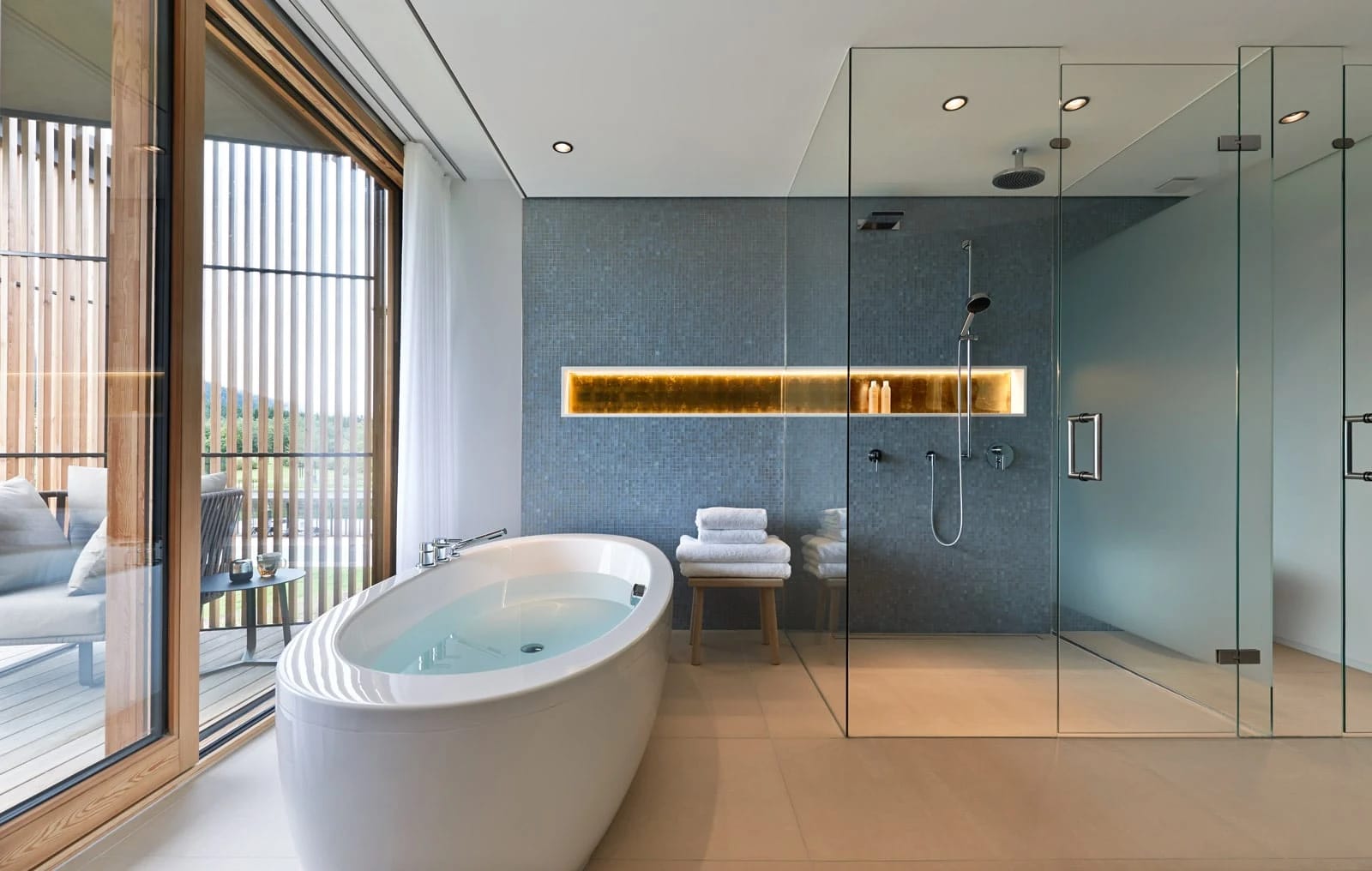 Badezimmer mit freistehender Badewanne, gläserner Regendusche und Fenster zum Balkon