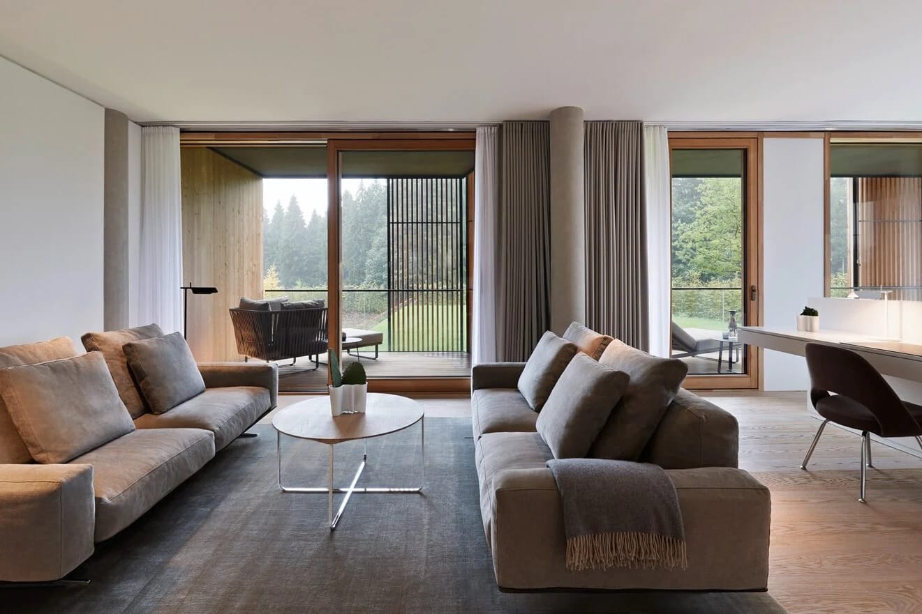 Großzügiger Wohnraum einer Suite mit zwei Sofas und raumhohen Fenstern zum Wald