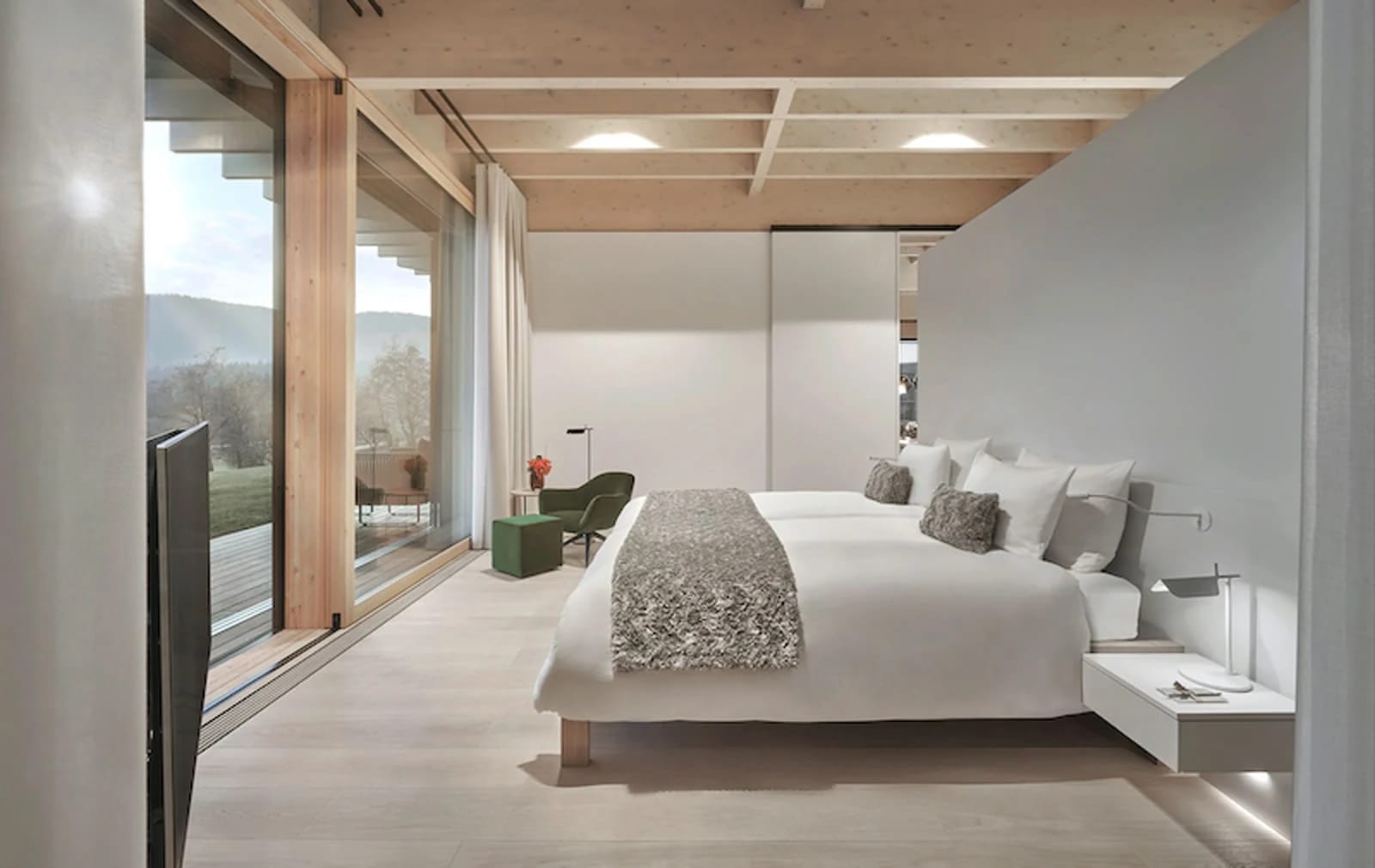 Schlafzimmer mit Holzbalkendecke, bodentiefen Fenstern und Zugang zum Balkon