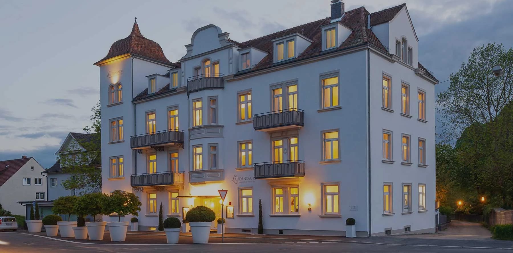 Weiße historische Hotelvilla mit Türmchen und beleuchteten Fenstern in der Abenddämmerung