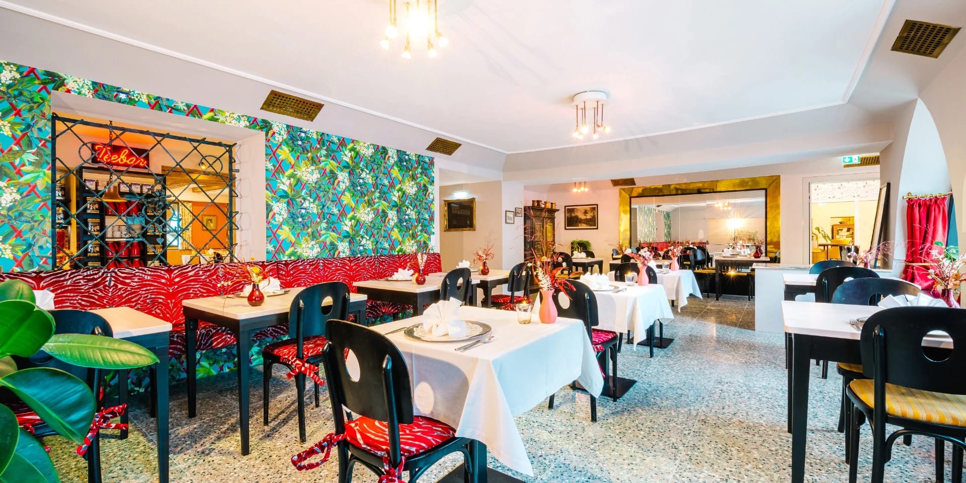 Speisesaal mit weiß eingedeckten Tischen, schwarz-roten Stühlen und floraler Wandtapete
