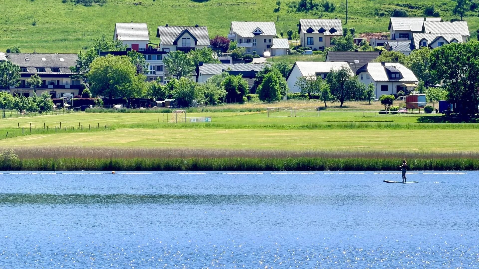 Sommerlicher Blick über den Meerfelder Maar auf den Ort mit Stand-up-Paddler