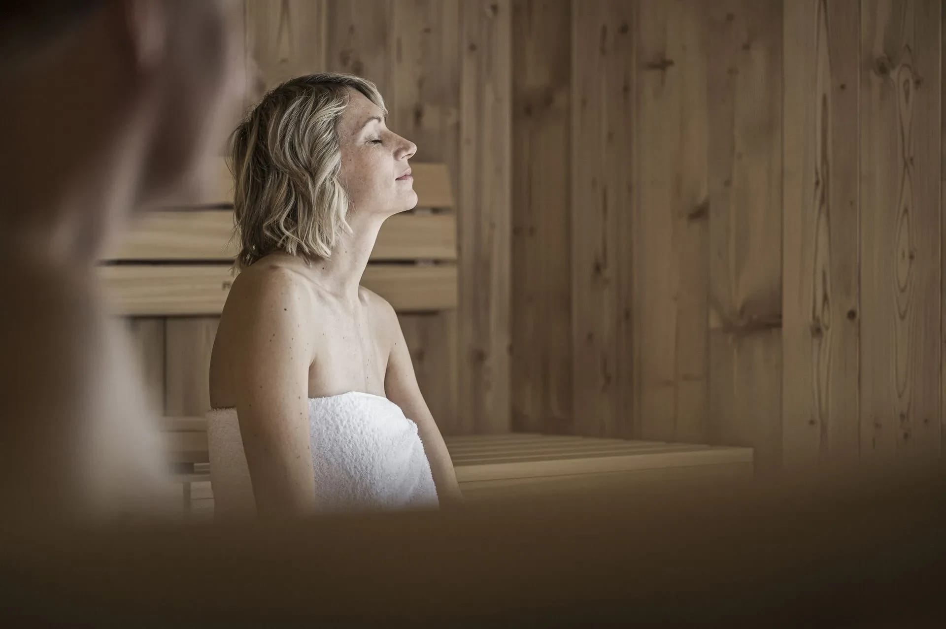 Holzsauna mit Sitzbänken, eine Frau sitzt entspannt im Handtuch
