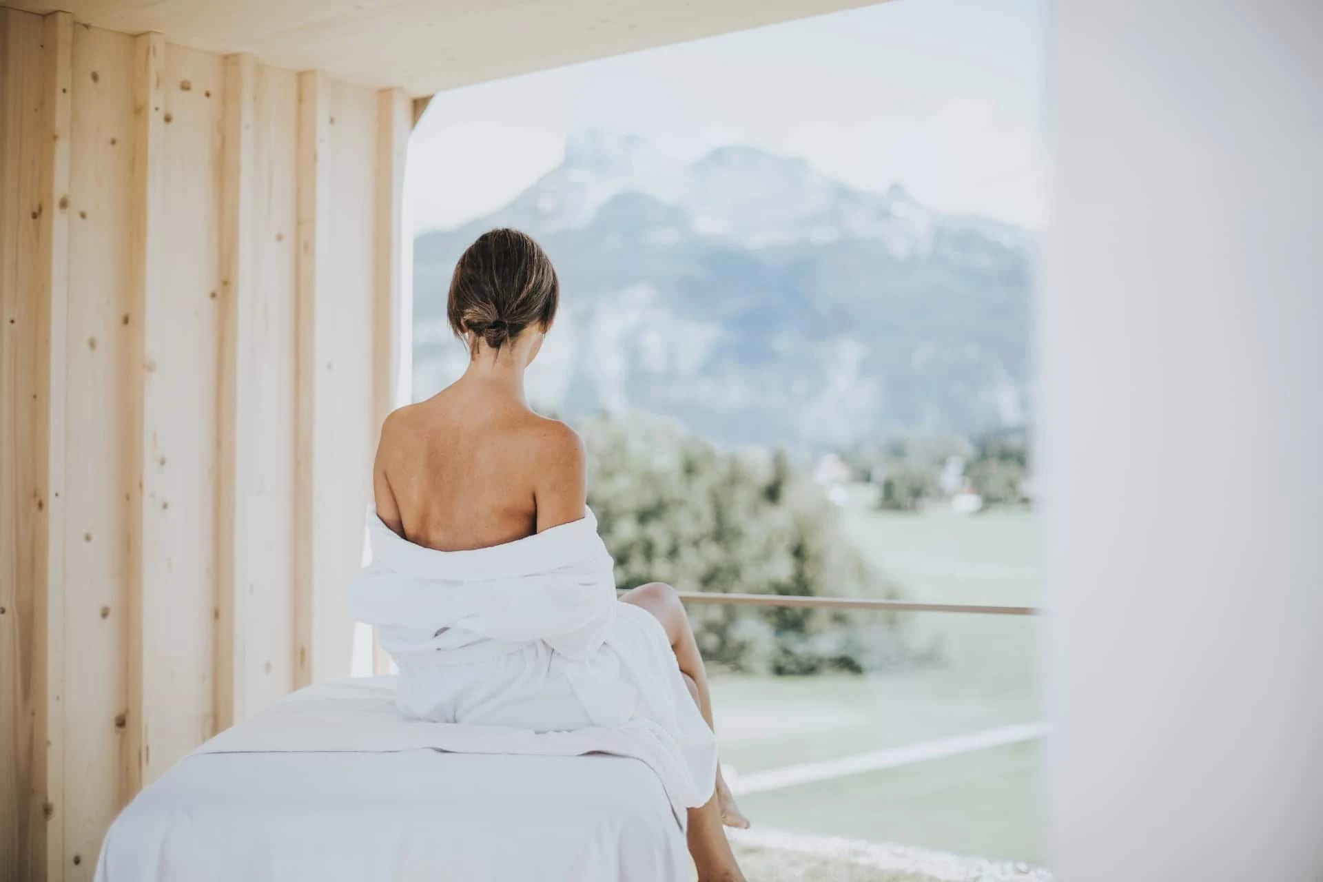 Frau in weißem Bademantel auf Wellnessliege mit Blick auf Bergpanorama im NABEL SPA