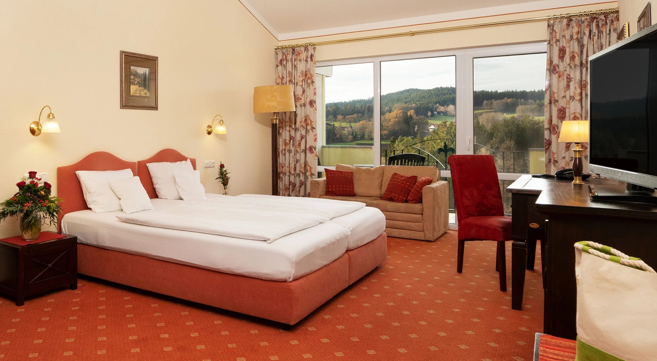 Luxuszimmer mit Doppelbett, Sofa und rotem Teppichboden vor großer Fensterfront