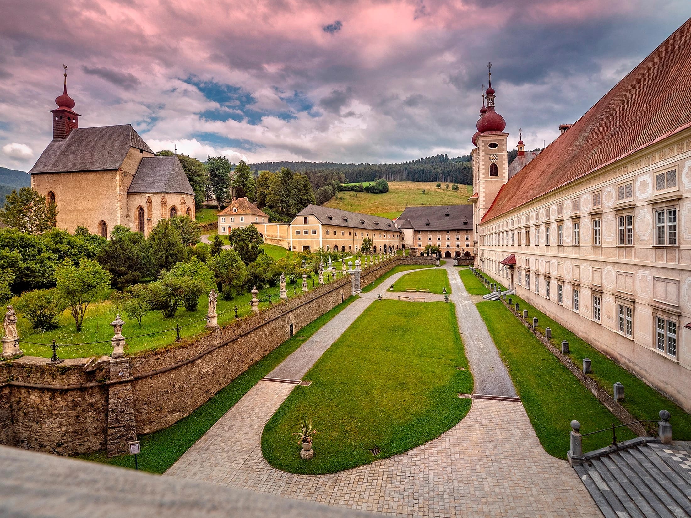 Blick von oben auf den Klostergarten mit Wegen, Stiftsmauer und Kirche im Abendhimmel