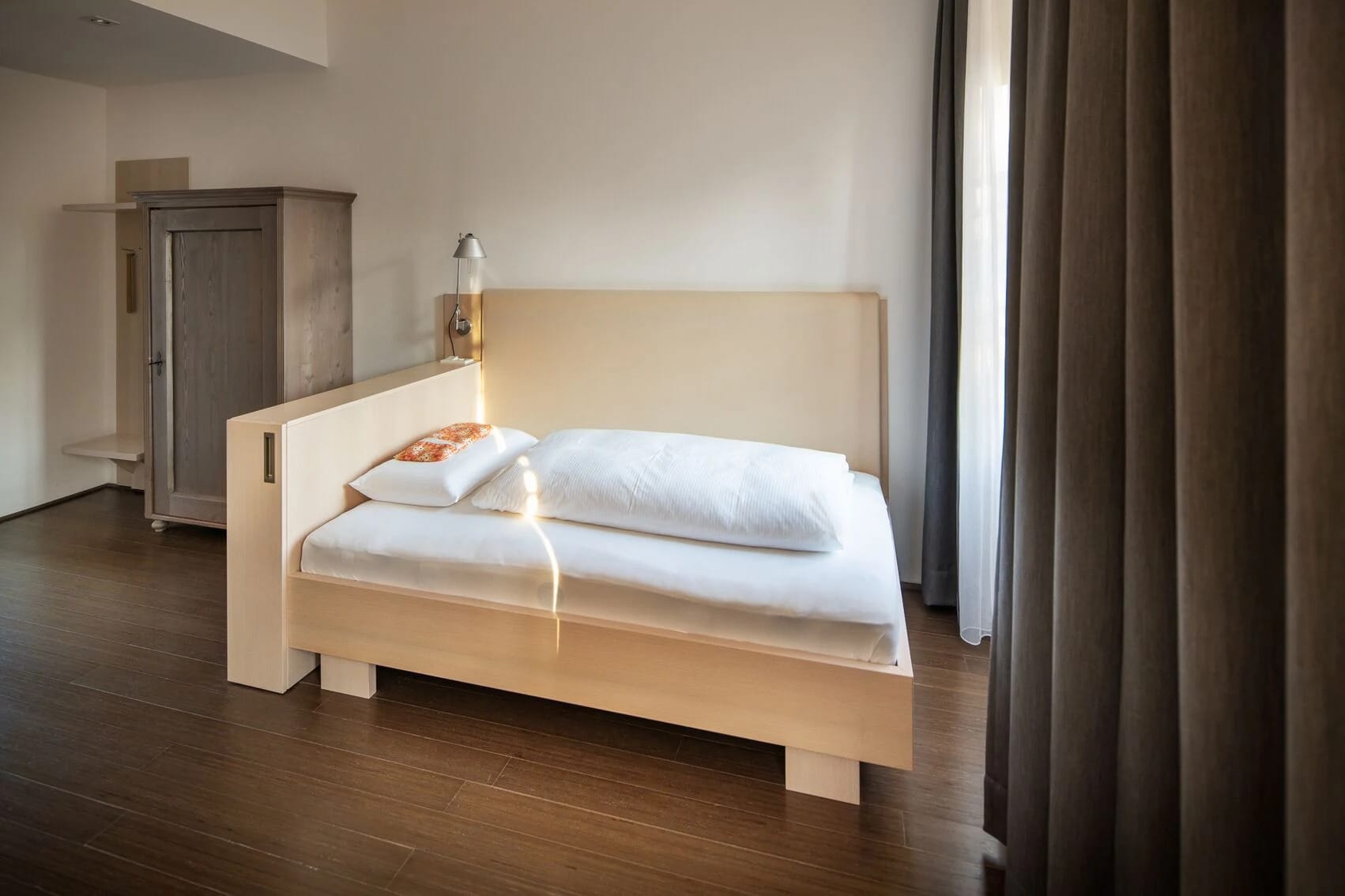Zimmer mit breitem Einzelbett aus hellem Holz und altem Bauernschrank