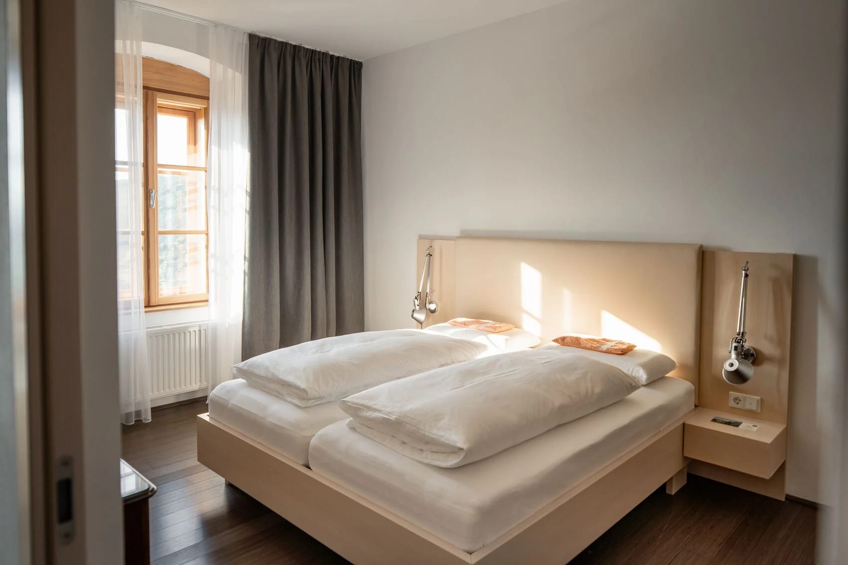 Doppelzimmer mit hellem Bett, Leselampen und Rundbogenfenster