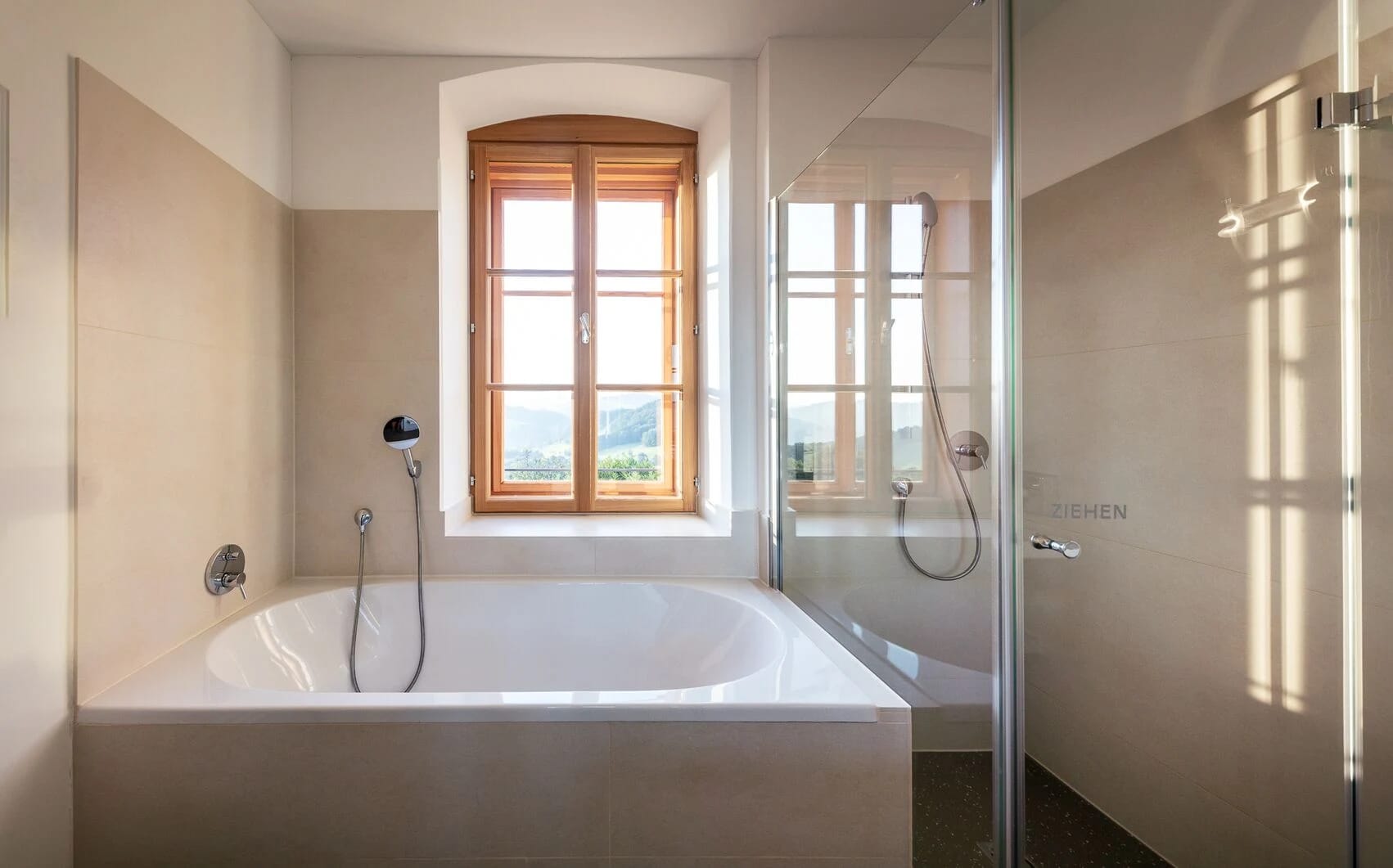 Helles Badezimmer mit Badewanne am Fenster und bodengleicher Dusche