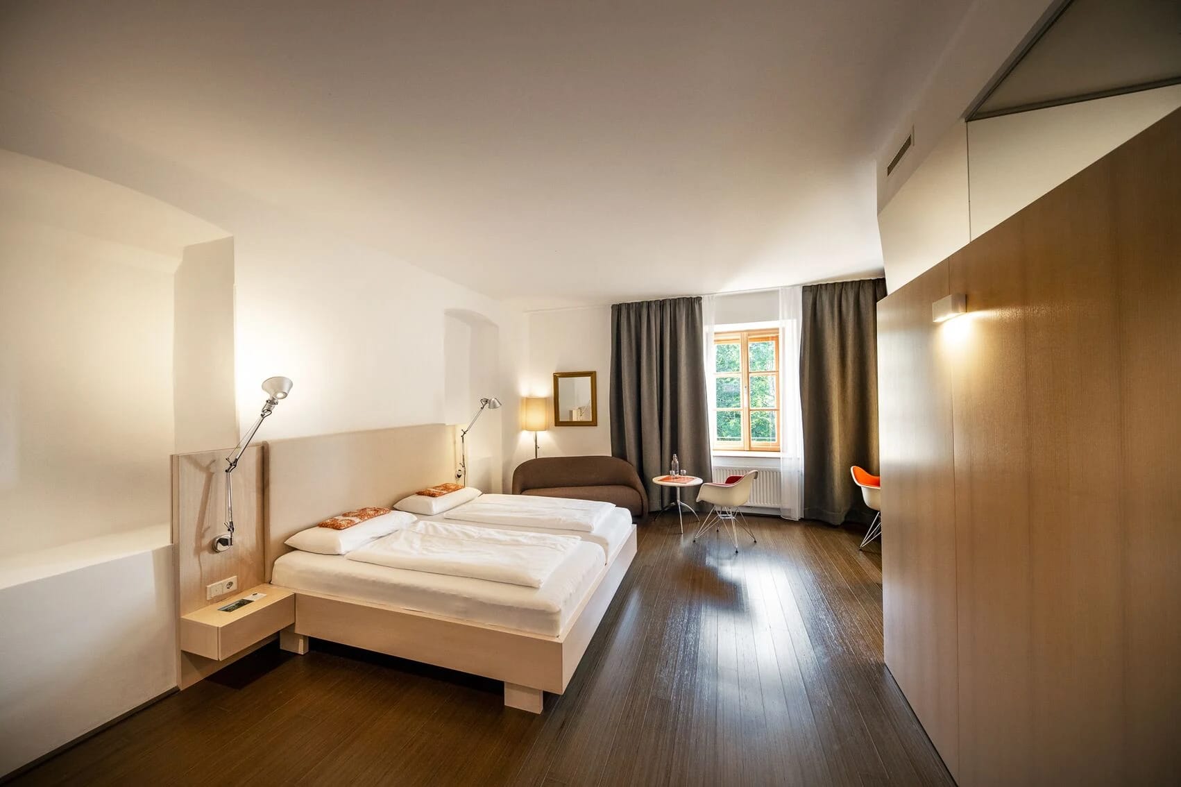 Geräumiges Doppelzimmer mit dunklem Holzboden, Sitzecke und Schreibtisch am Fenster