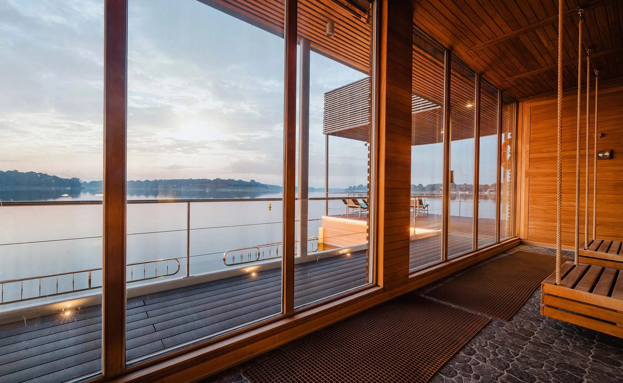Holzverkleideter Innenraum der Seesauna mit raumhohen Fenstern, Terrasse und Blick über den See