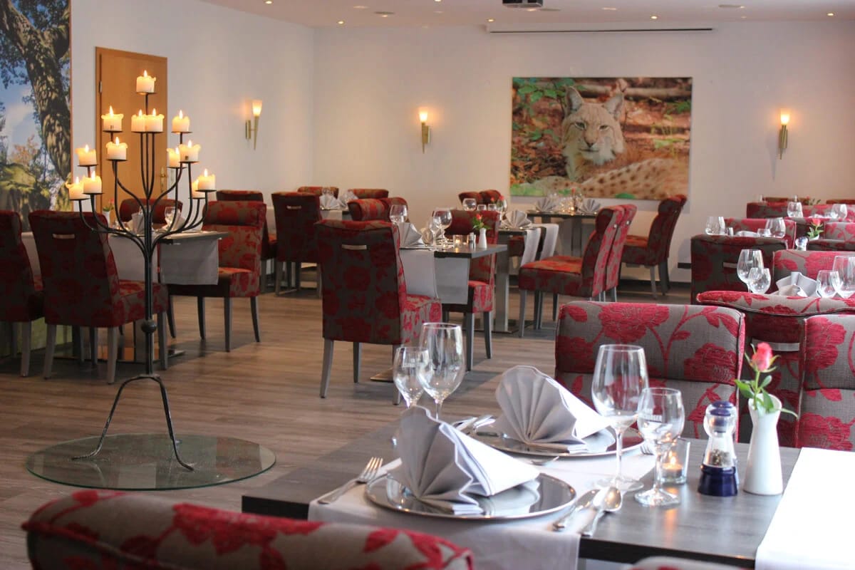 Restaurant mit eingedeckten Tischen, rot gemusterten Polsterstühlen und großem Kerzenleuchter