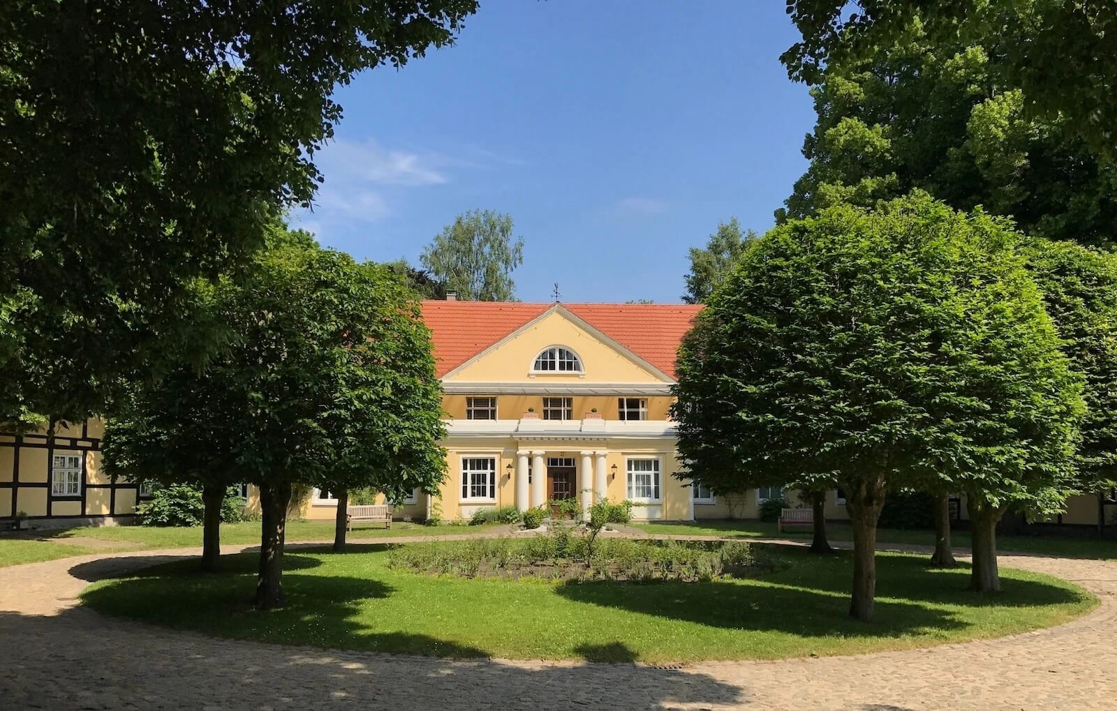 Gutshaus hinter einer Baumallee mit Blick über den gepflasterten Innenhof