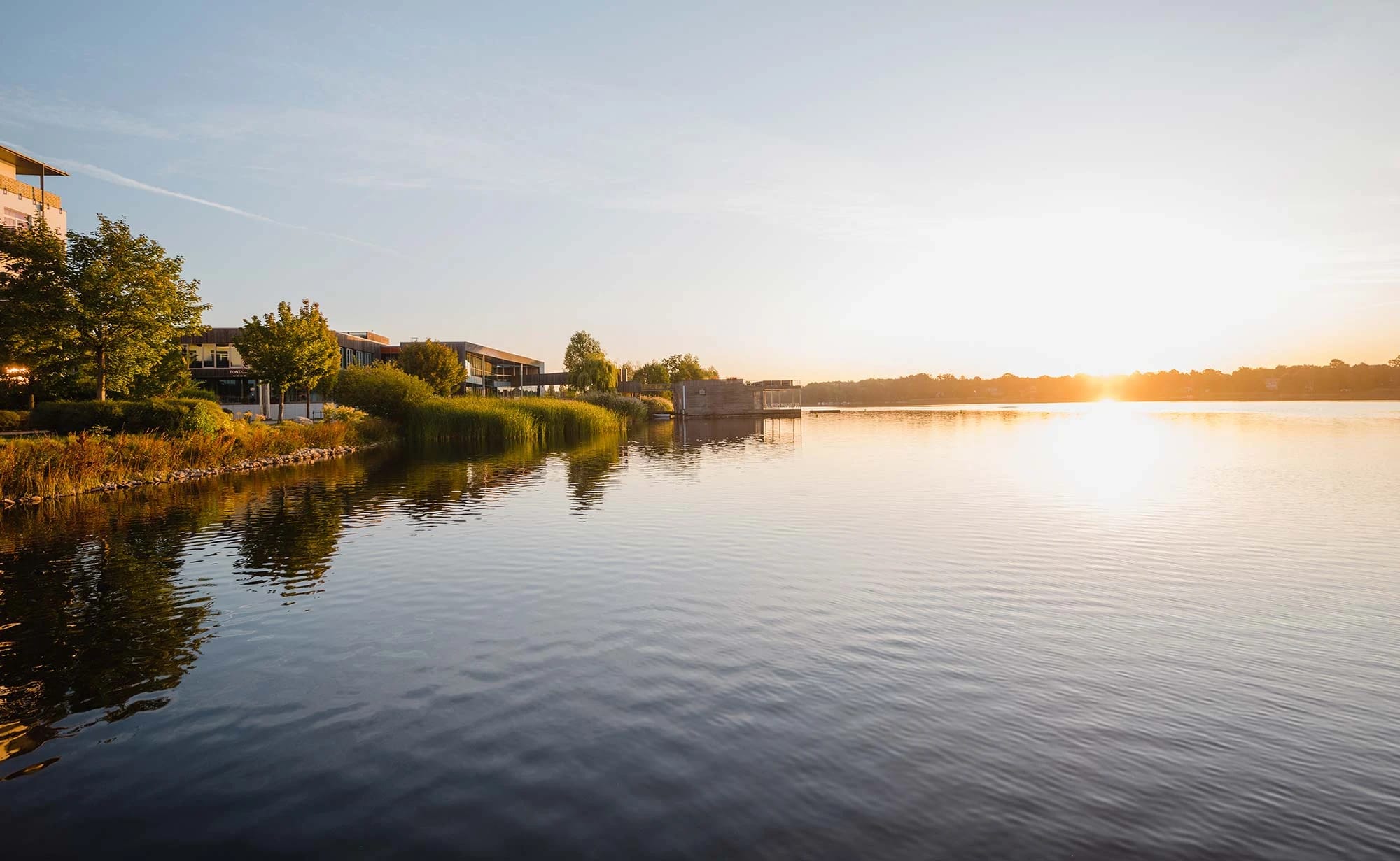 Sonnenuntergang über dem Ruppiner See, am linken Ufer die Gebäude des Resorts zwischen Bäumen
