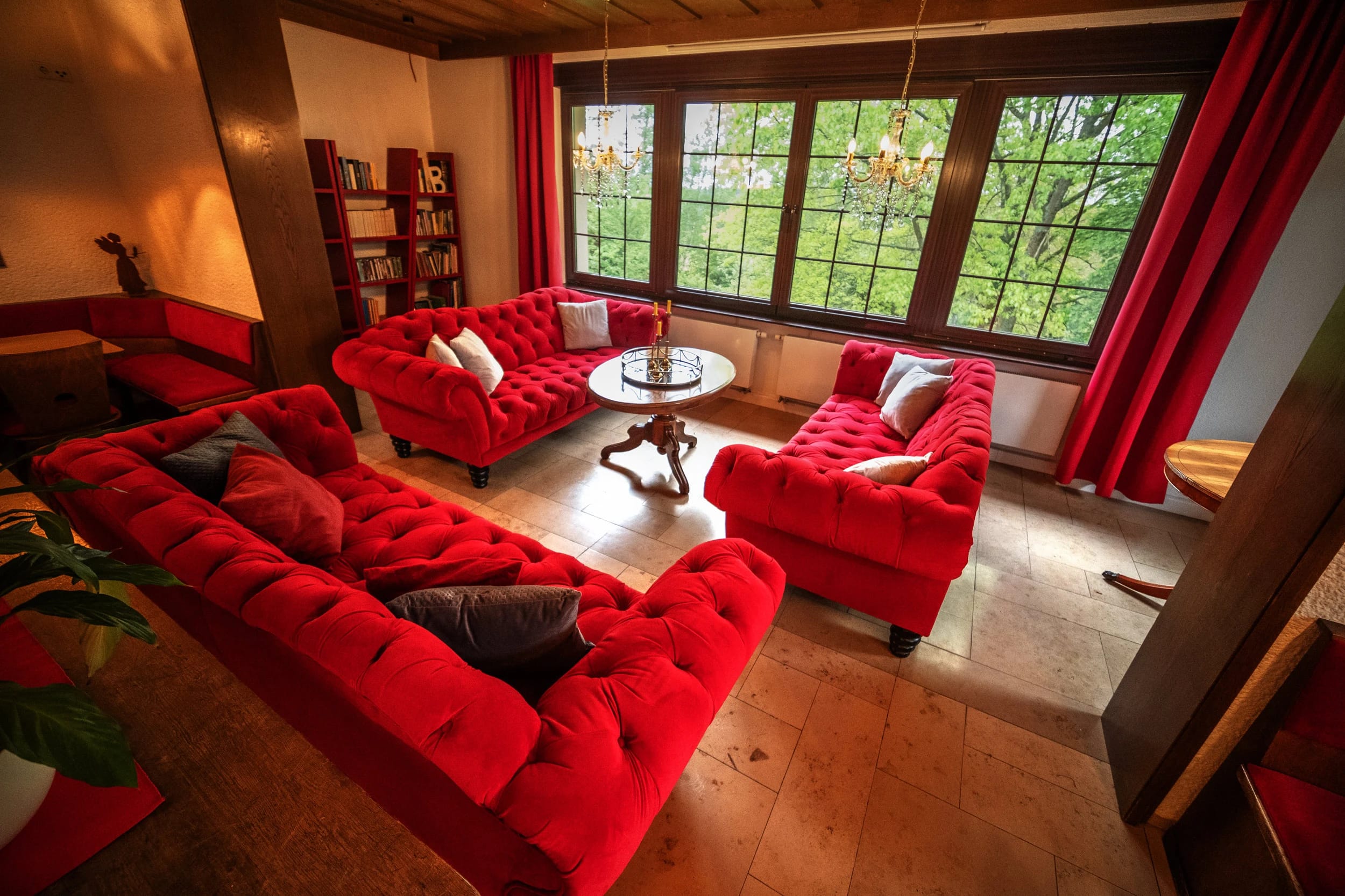 Salon mit roten Samtsofas, Bücherregal und Sprossenfenstern