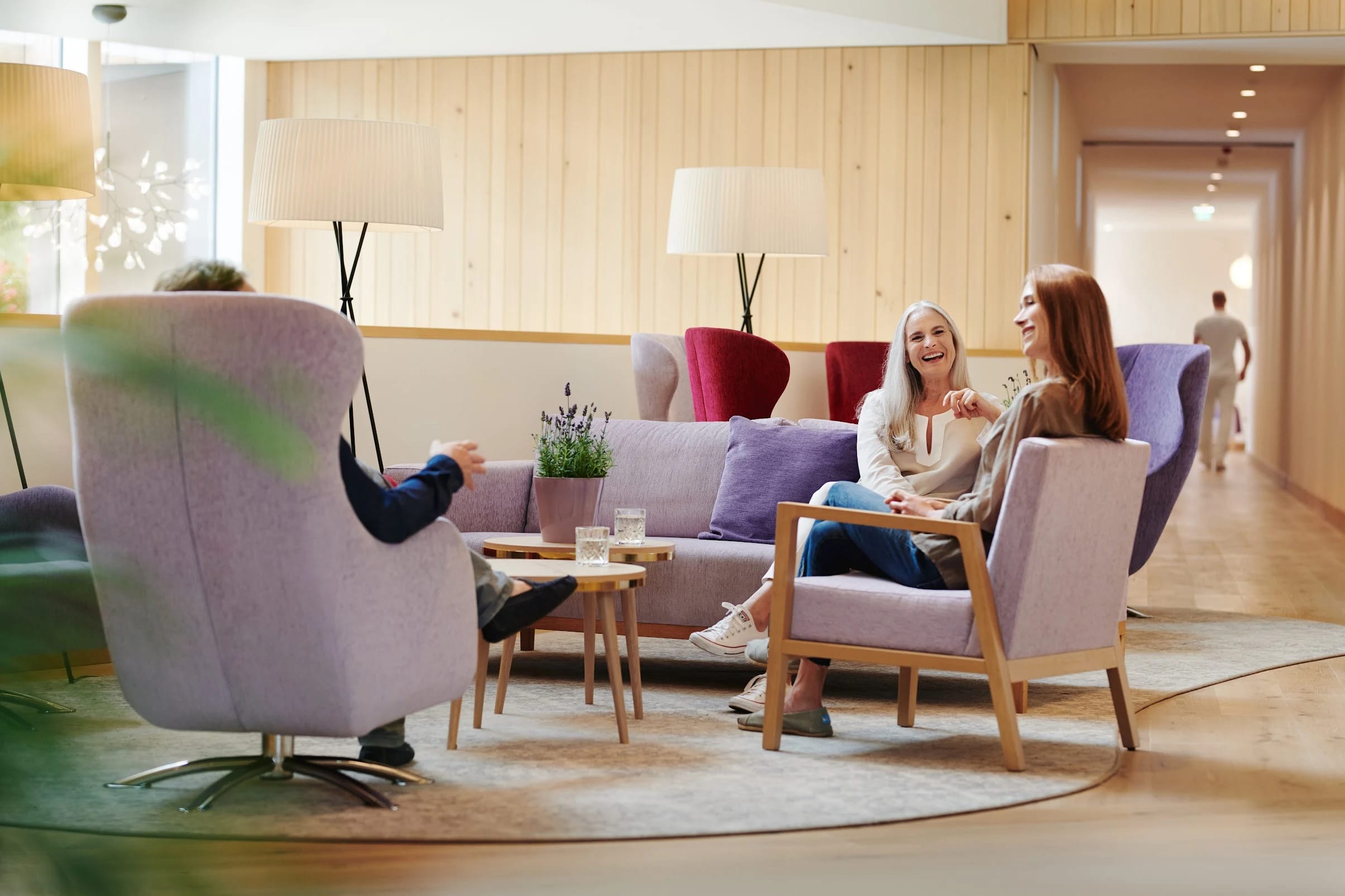 Lounge mit fliederfarbenem Sofa, Sesseln, Stehlampen und Holzverkleidung