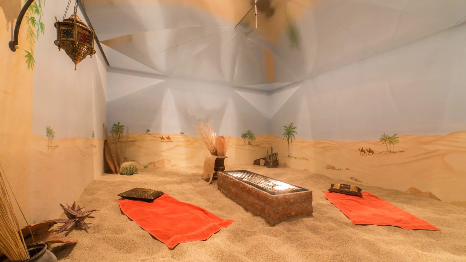 Sandlichtbad mit Wüstenmalerei an der Wand, Sandboden und roten Liegetüchern