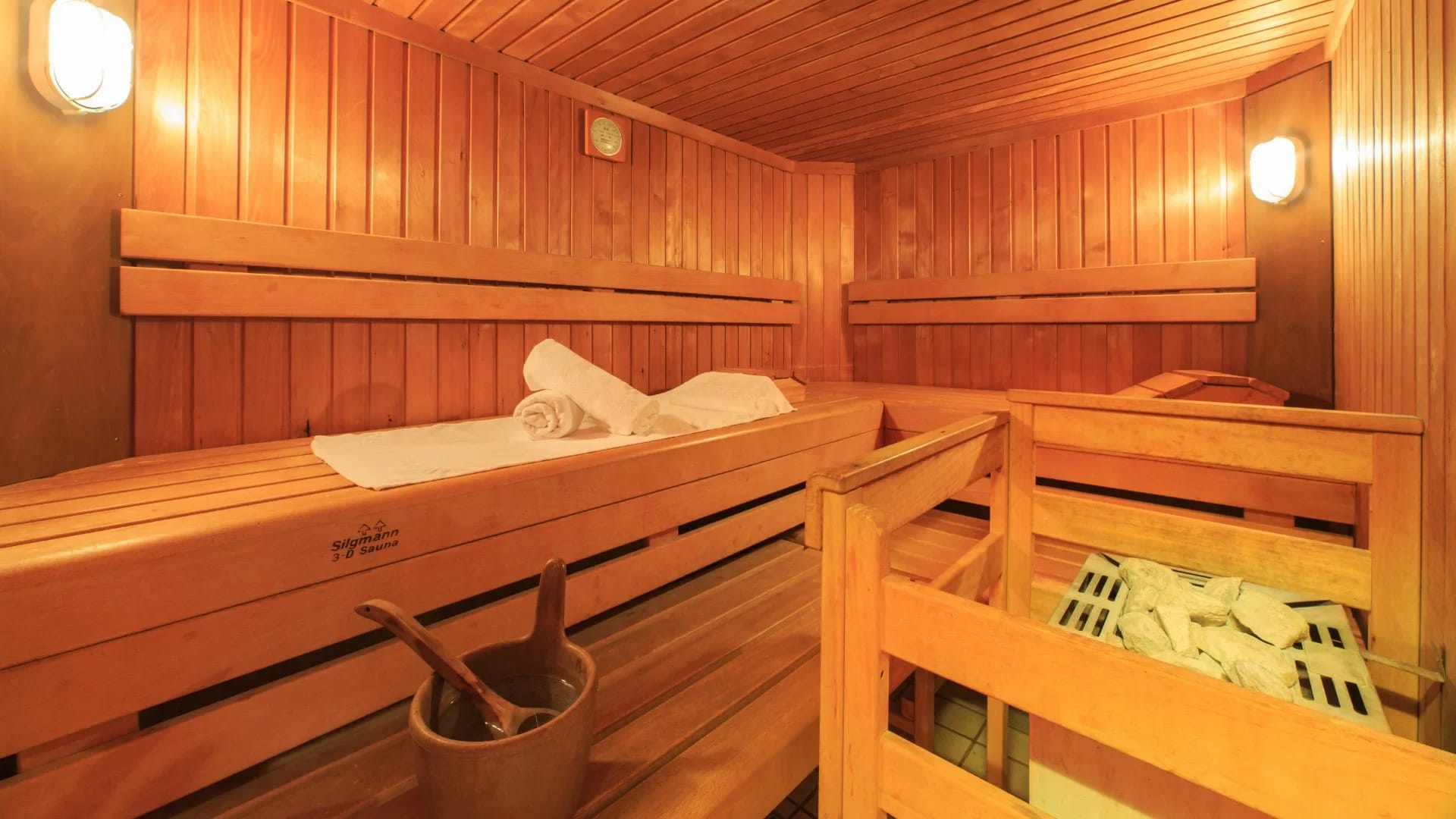 Holzsauna mit Bänken, gerollten Handtüchern, Aufgusskübel und Saunaofen