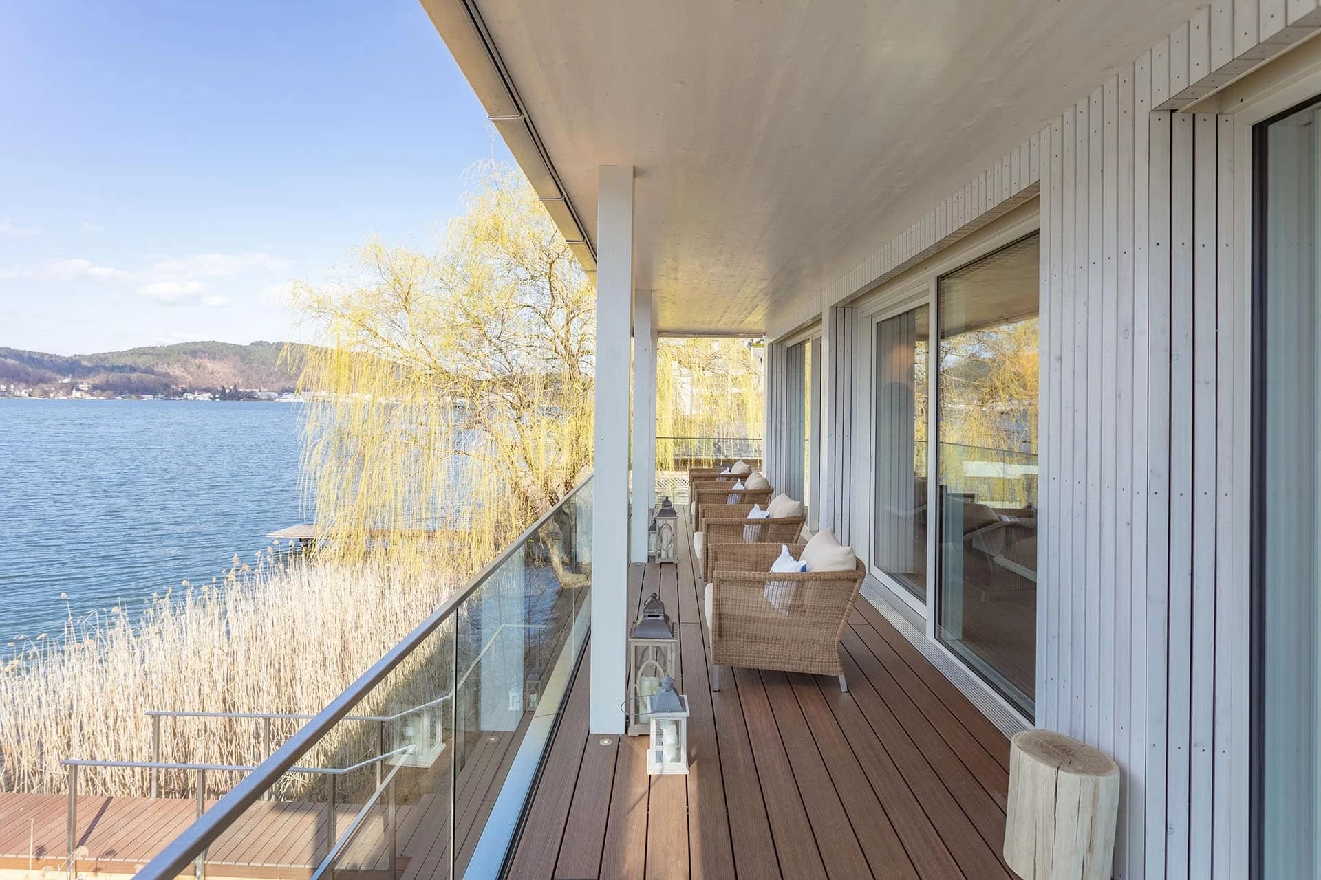 Holzbalkon mit Sesseln und Glasgeländer über dem See