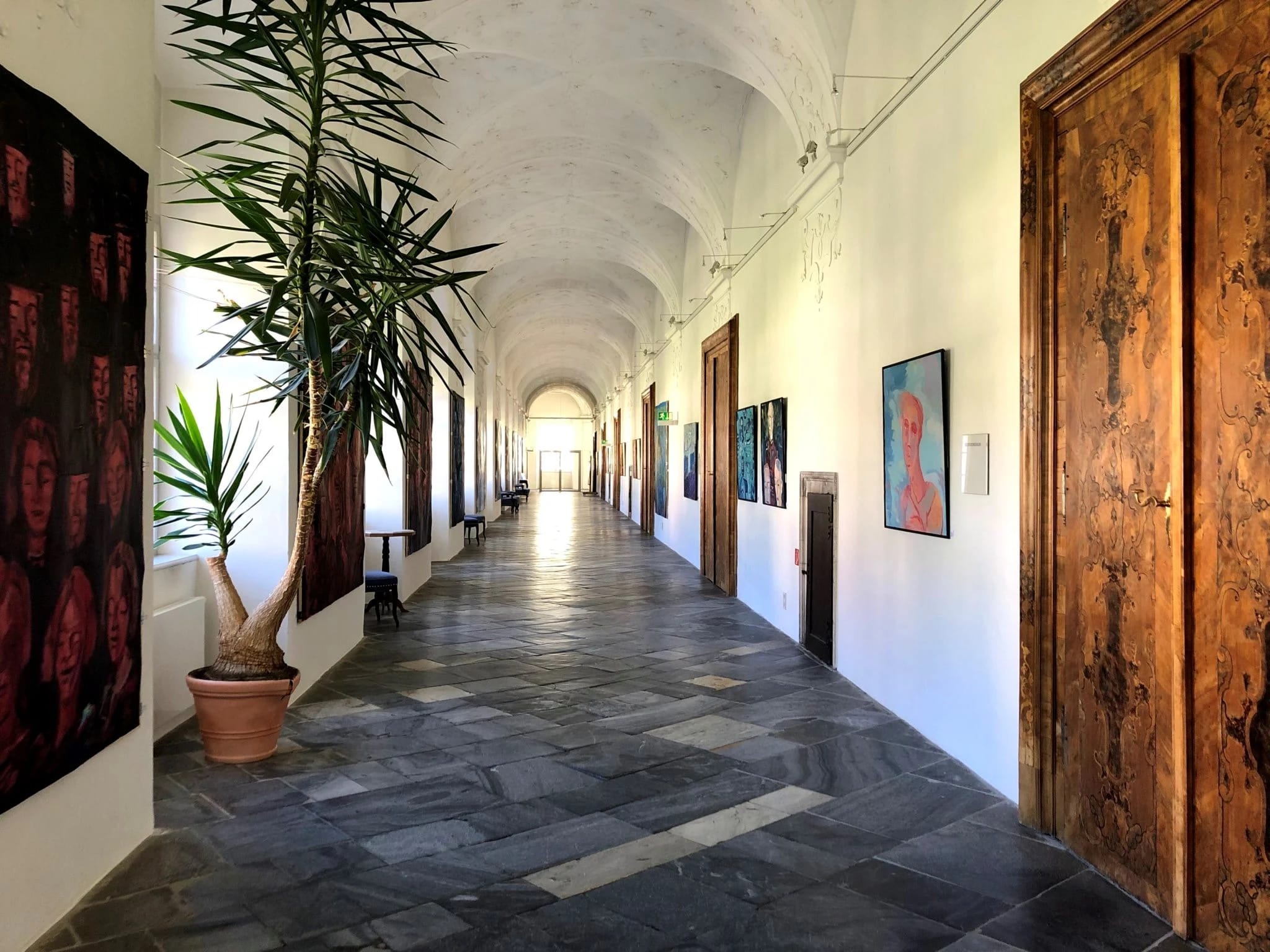 Langer Gewölbegang mit Schieferboden, Holztüren, Zimmerpflanze und moderner Kunst an den Wänden