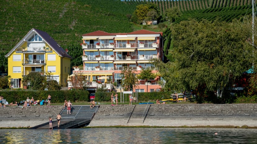 Das Hotel vom Bodensee aus gesehen, davor der Badestrand, dahinter Weinberge