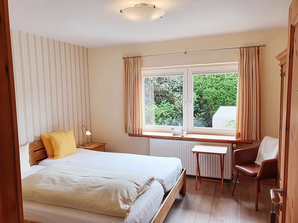 Zimmer mit Bett, Nachttisch, kleinem Schreibtisch und Ledersessel am Fenster