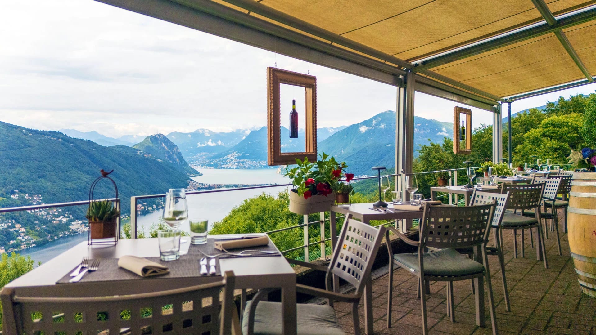 Überdachte Restaurantterrasse mit eingedeckten Tischen und Blick auf den Luganersee