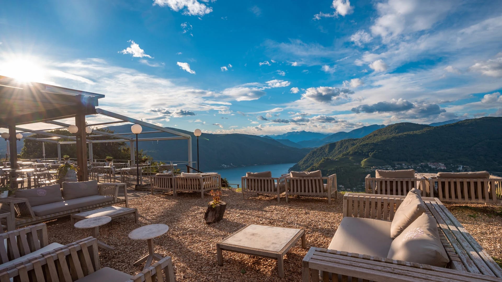 Terrasse mit Loungesesseln unter Pergola und weitem Blick auf See und Berge